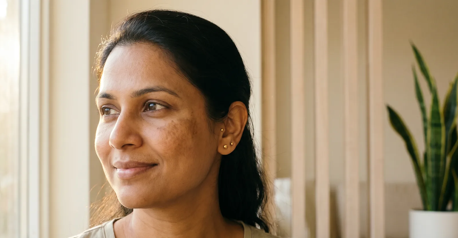 Indian woman with soft natural melasma across the cheeks, calm dignified portrait in warm afternoon light.
